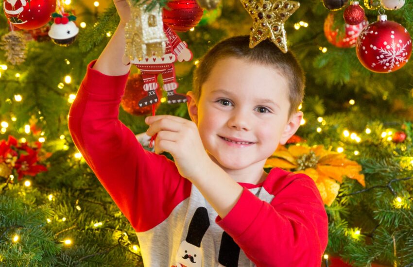 Little boy decorated as a Christmas tree while decorating a Christmas tree