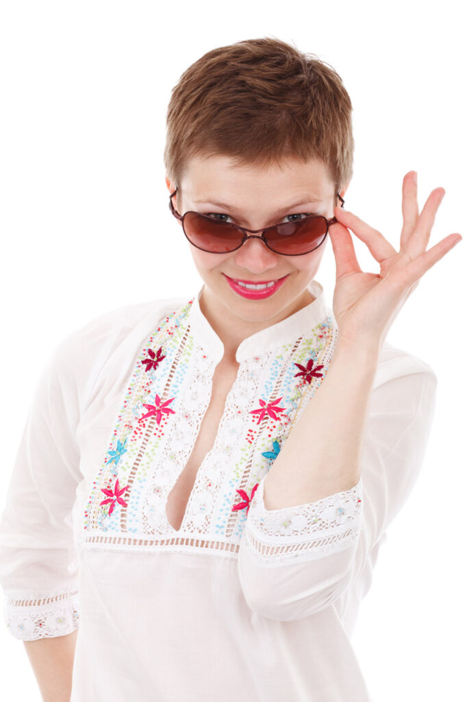 Woman wearing sunglasses while peering above the and smiling